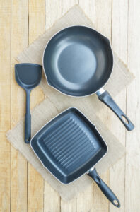 Non-stick frying pan and grill pan with spatula on wooden surface for healthy cooking