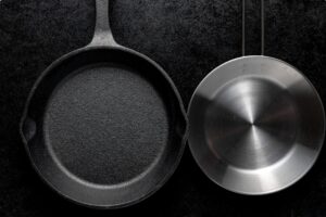 Cast iron skillet and stainless steel pan side by side on dark background comparison