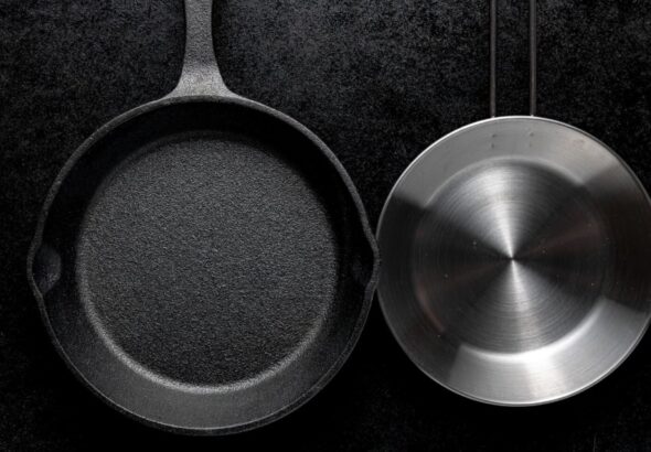 Cast iron skillet and stainless steel pan side by side on dark background comparison