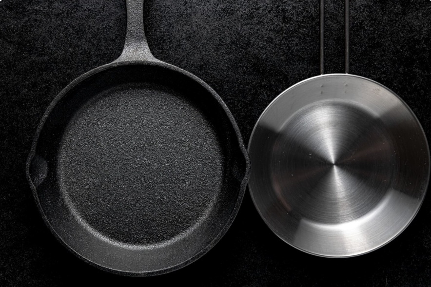 Cast iron skillet and stainless steel pan side by side on dark background comparison