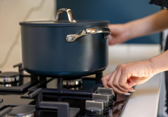 Person adjusting a gas stove knob with a Dutch oven pot cooking on the burner.