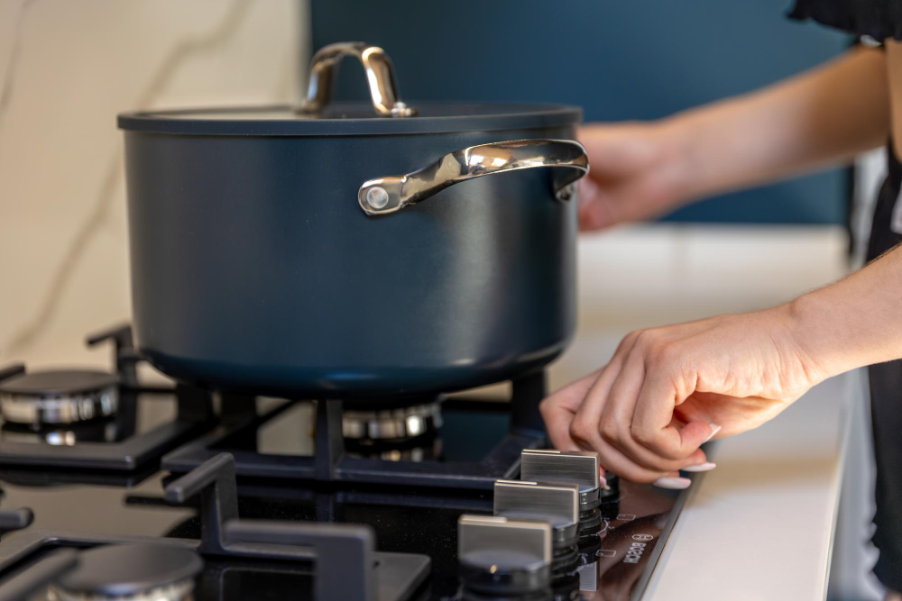 Person adjusting a gas stove knob with a Dutch oven pot cooking on the burner.