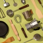 Top kitchen essentials including frying pan, whisk, ladle, rolling pin, strainer, and coffee maker on green background