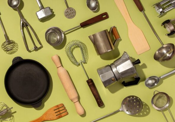 Top kitchen essentials including frying pan, whisk, ladle, rolling pin, strainer, and coffee maker on green background