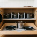 Organized kitchen cabinet with hanging cast iron skillets, dividers for pots, and a pull-out drawer with pans