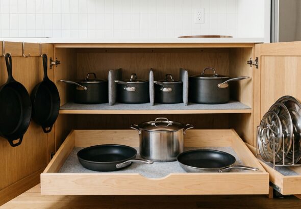 Organized kitchen cabinet with hanging cast iron skillets, dividers for pots, and a pull-out drawer with pans